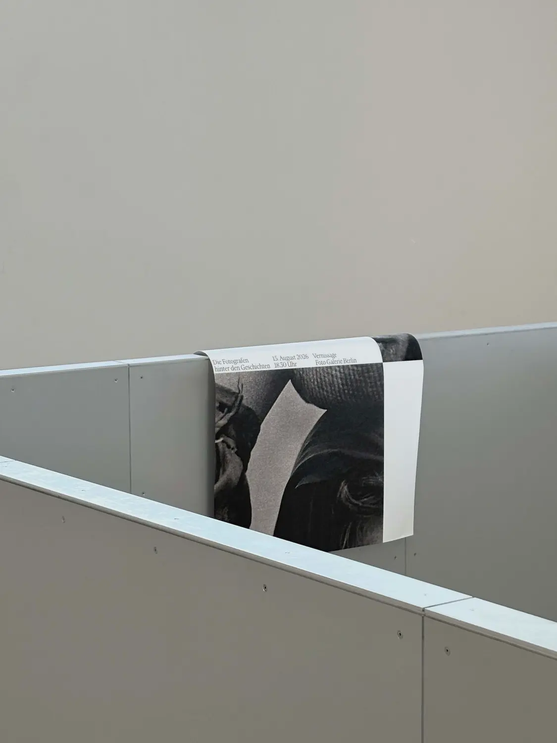 An exhibition poster draped over a gray metal partition